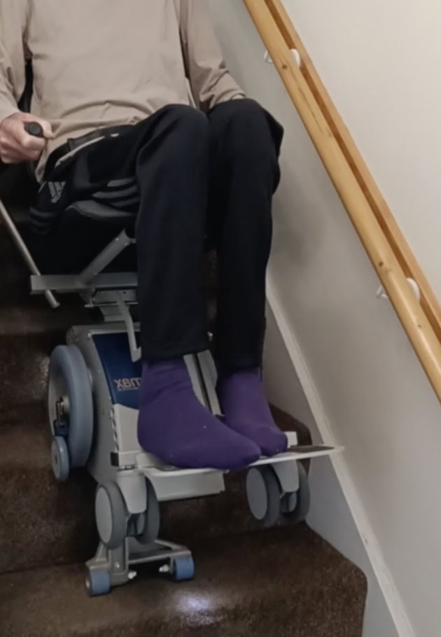 elderly man comes downstairs. He is sat on a stairclimber as he has reduced mobility